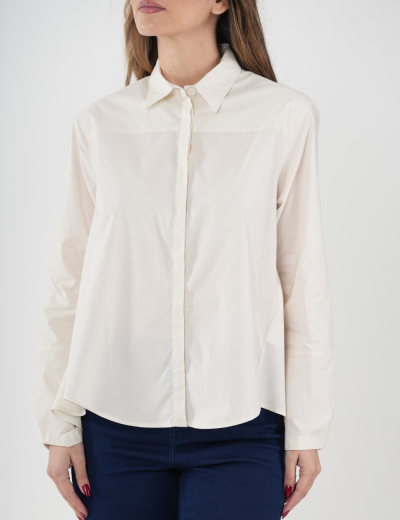 Camisa feminina creme de manga comprida com gola clássica e botões frontais, sobre calças jeans azuis em fundo branco.