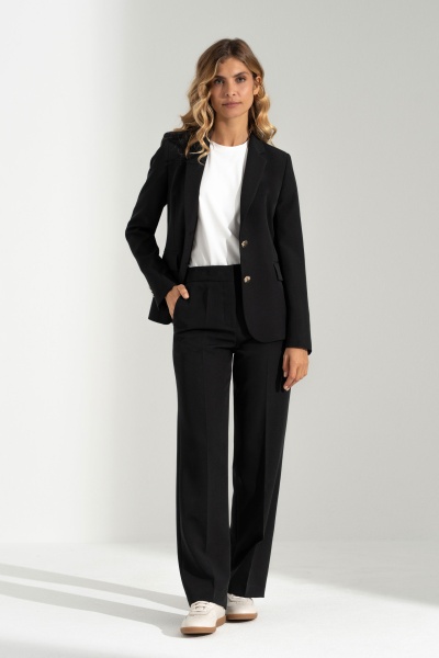 Mulher vestindo fato feminino preto e camisa branca com ténis brancos.