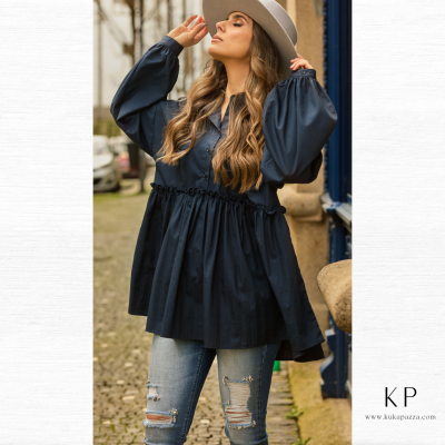 Mulher com veste azul escura de mangas bufantes, jeans rasgados e chapéu bege ao ar livre na rua.