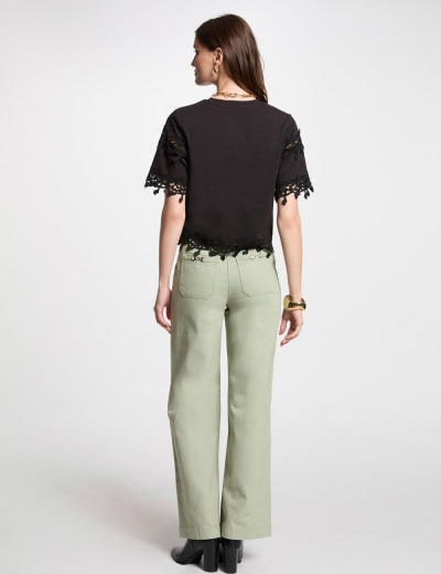 Mulher de costas com t-shirt preta com renda, calças verdes largas e sapatos pretos