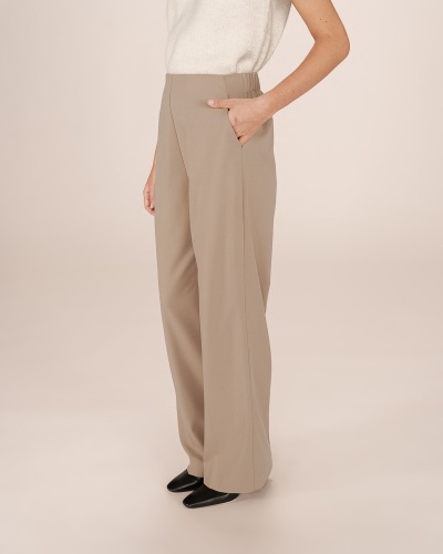 Calças largas bege com bolso lateral, blusa branca e sapatos pretos num fundo branco