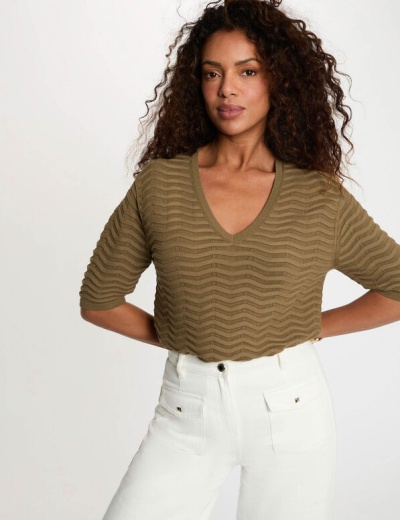 Mulher com top verde texturizado e calças brancas com bolsos frontais