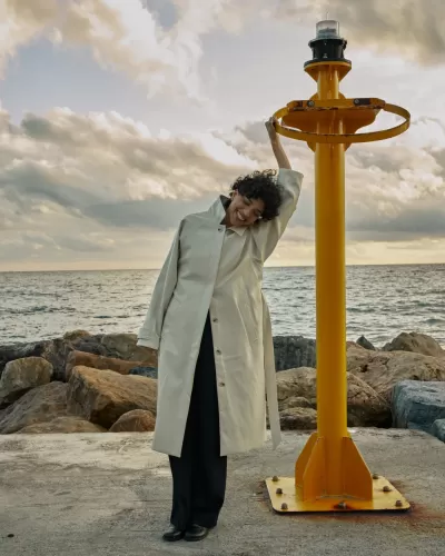 Mulher com casaco creme junto ao mar e estrutura amarela