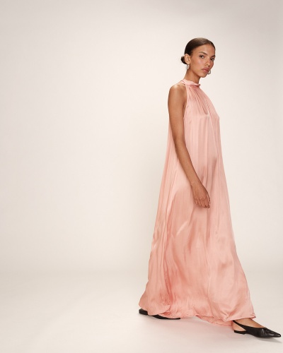 Vestido comprido cor-de-rosa fluído de gola alta e sem mangas com sapatos pretos, mulher de cabelo apanhado.