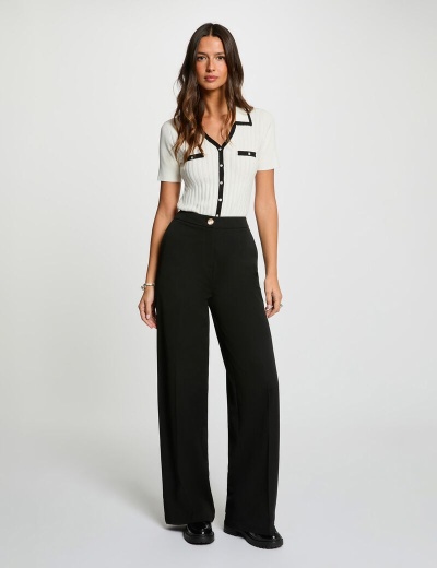 Mulher a usar camisa branca com detalhes pretos e calças largas pretas