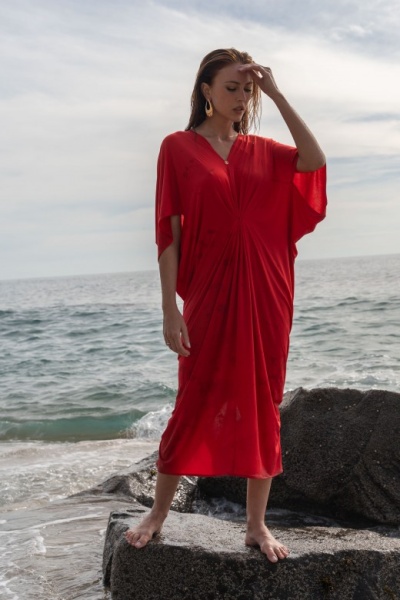 Mulher com vestido vermelho comprido com decote em V em cima de rochas junto ao mar