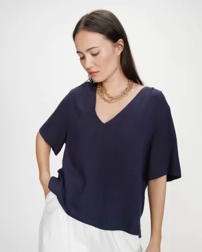 Mulher com t-shirt azul marinho de manga curta e decote em V, calças brancas e colar dourado