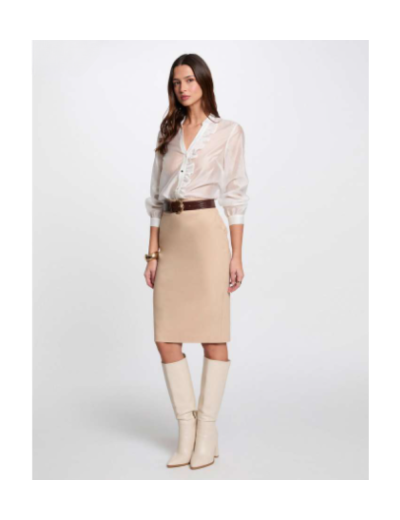 Mulher com camisa branca semi-transparente, saia lápis bege, cinto castanho e botas bege.