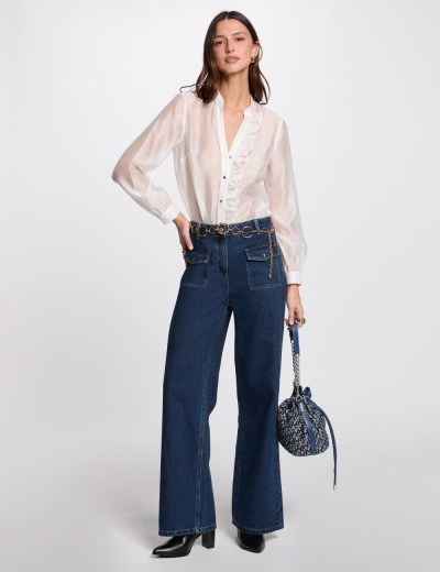 Mulher com camisa branca semitransparente, calças de ganga azul, botas pretas e mala mochila azul