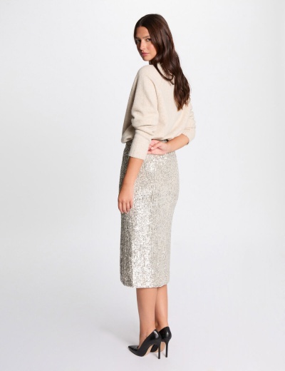 Mulher com saia lápis prateada, camisola creme e sapatos pretos de salto alto em fundo branco