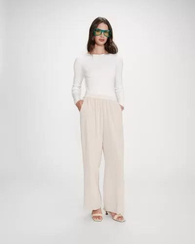 Mulher com camisola branca, calças largas bege, sandálias claras e óculos de sol verdes.