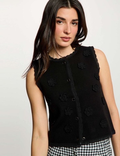 Top feminino preto com botões, renda e flores aplicadas, usado com calças xadrez.