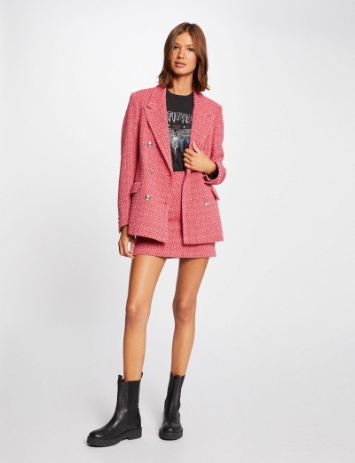 mulher a usar casaco rosa, saia rosa, t-shirt preta e botas pretas