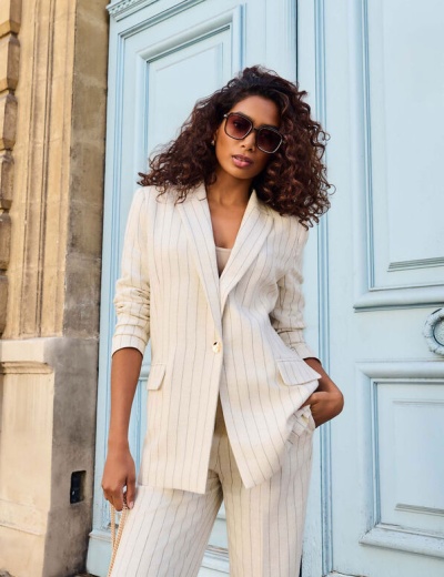 Mulher com fato claro riscado e óculos de sol junto a uma porta azul clara