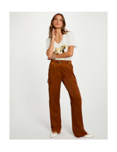 Mulher com t-shirt branca com padrão dourado e calças castanhas largas