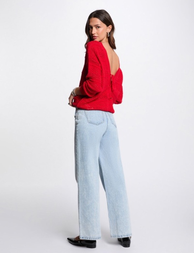 Mulher vestindo camisola vermelha de malha com costas abertas e calças de ganga claras