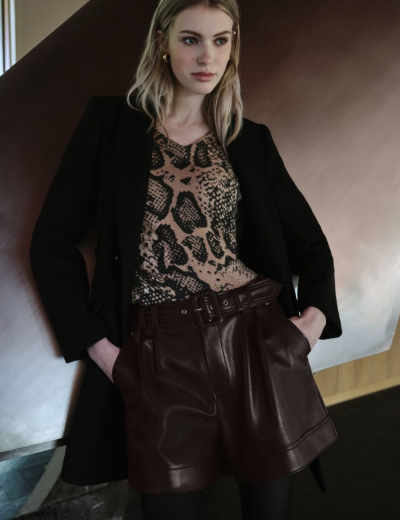 Mulher com casaco preto, camisa animal print e calções de couro castanho escuro