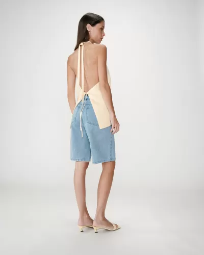 Mulher a usar top amarelo claro sem costas, calções de ganga azul clara e sandálias amarelas.