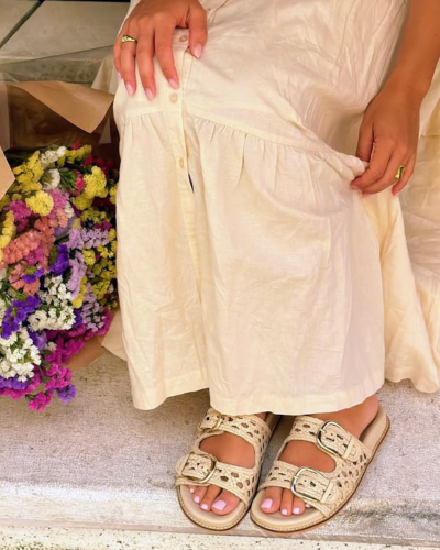 Sandálias bege trançadas com fivelas e vestido creme junto a flores coloridas