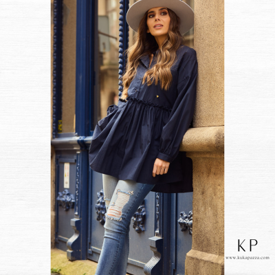 Mulher com blusa azul escura, jeans rasgado e chapéu bege em cenário urbano