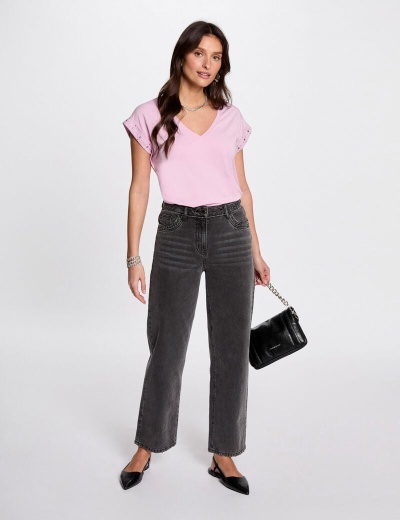 Mulher com t-shirt rosa, calças de ganga cinzentas e mala preta em fundo branco