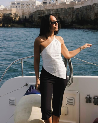 Mulher com top branco assimétrico e calças pretas em barco no mar
