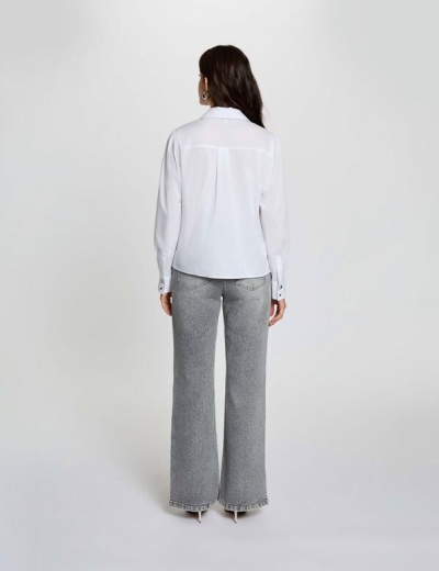 Mulher de costas com camisa branca de manga comprida e calças de ganga cinza