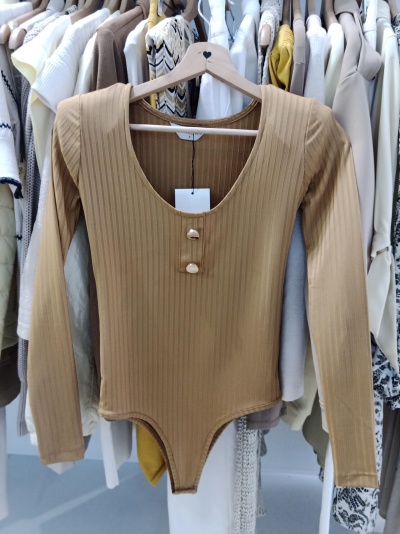 Body de malha canelada castanho com botões num cabide de madeira rodeado de roupa