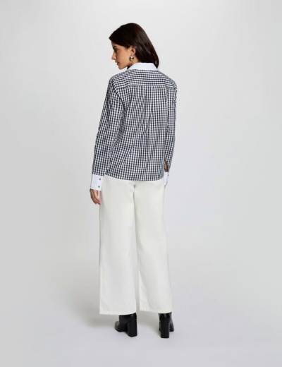 Mulher de costas com camisa xadrez preta e branca e calças brancas largas