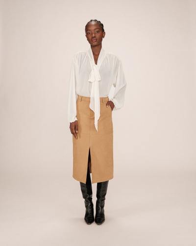 Conjunto feminino com blusa branca de tecido leve e saia camel midi com fenda, botas pretas altas.