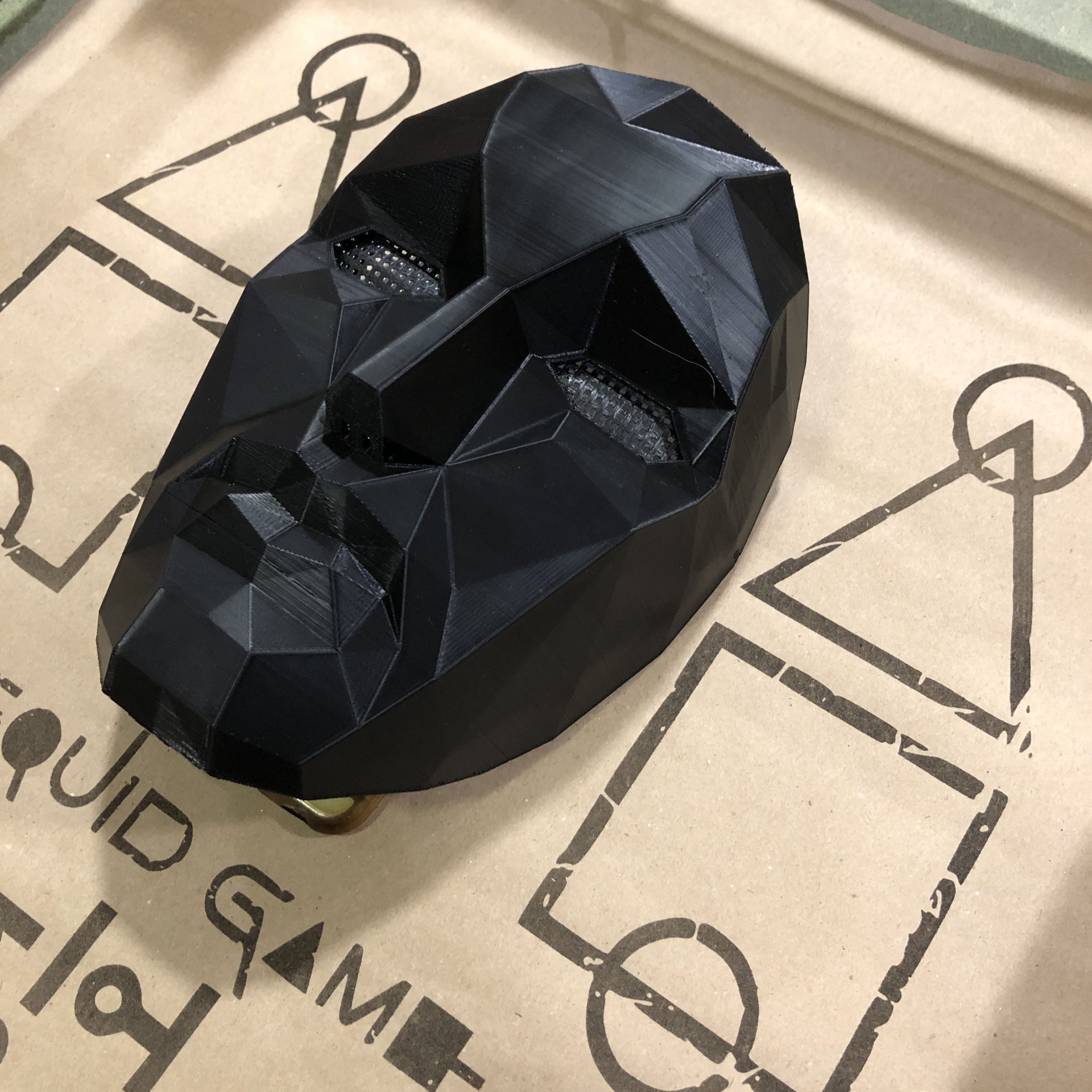 Serviço de Impressão 3D Personalizada – Transforme seus Modelos Digitais em Realidade Máscara preta facetada geométrica sobre papel castanho com texto e desenhos em preto