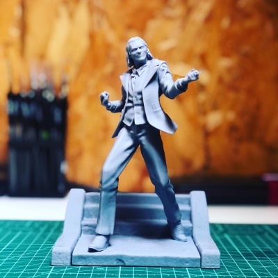 Estátua cinzenta de personagem masculino em pose dinâmica sobre base retangular