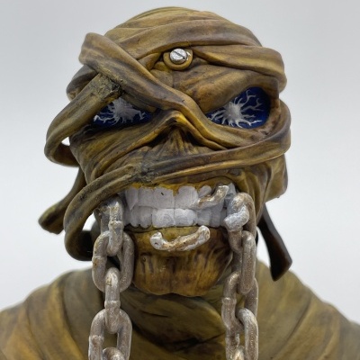 Figura de ação do Enigma da banda Iron Maiden com bandagens, olhos azuis e correntes na boca.