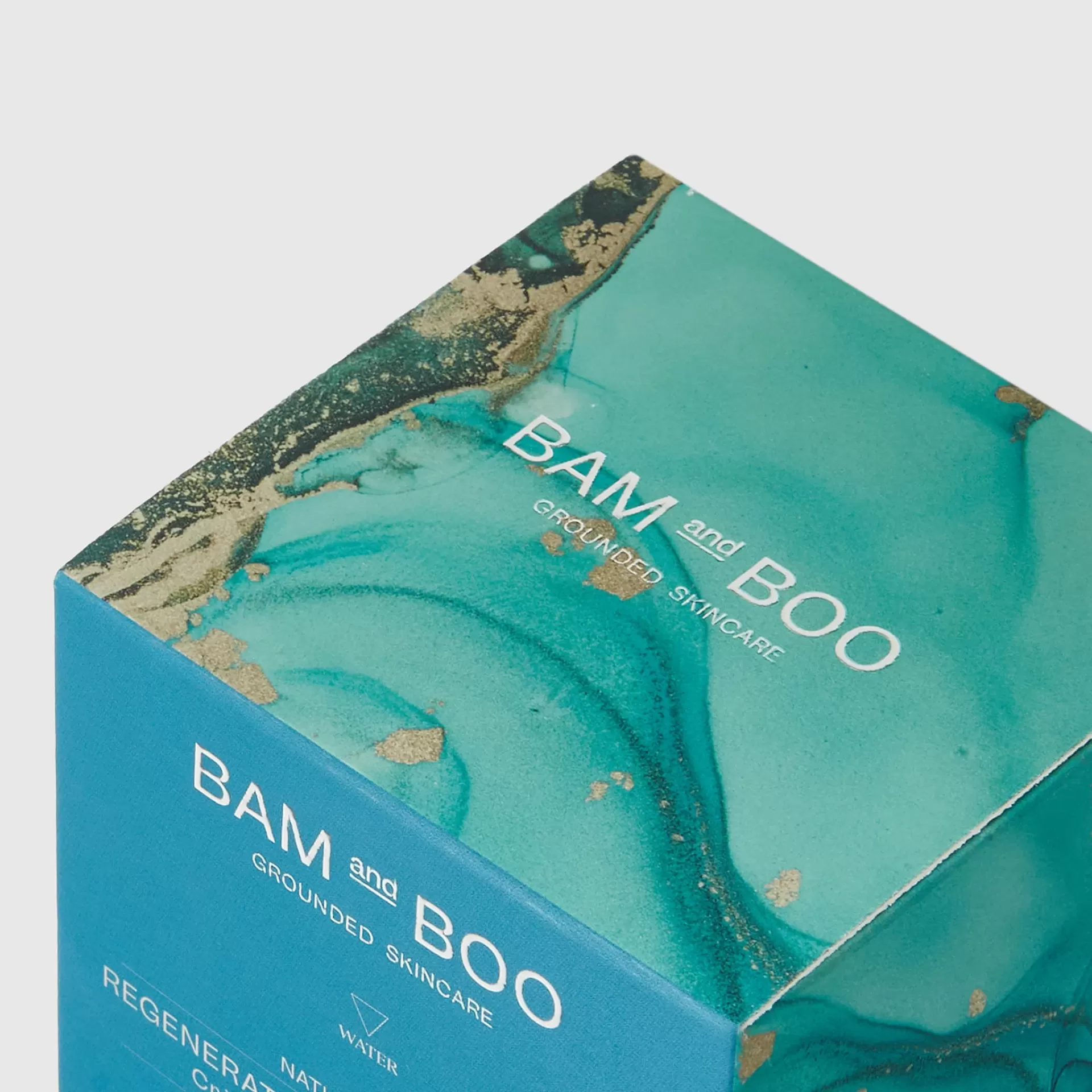 Embalagem azul com detalhes verdes e dourados, texto branco BAM and BOO GROUNDED SKINCARE