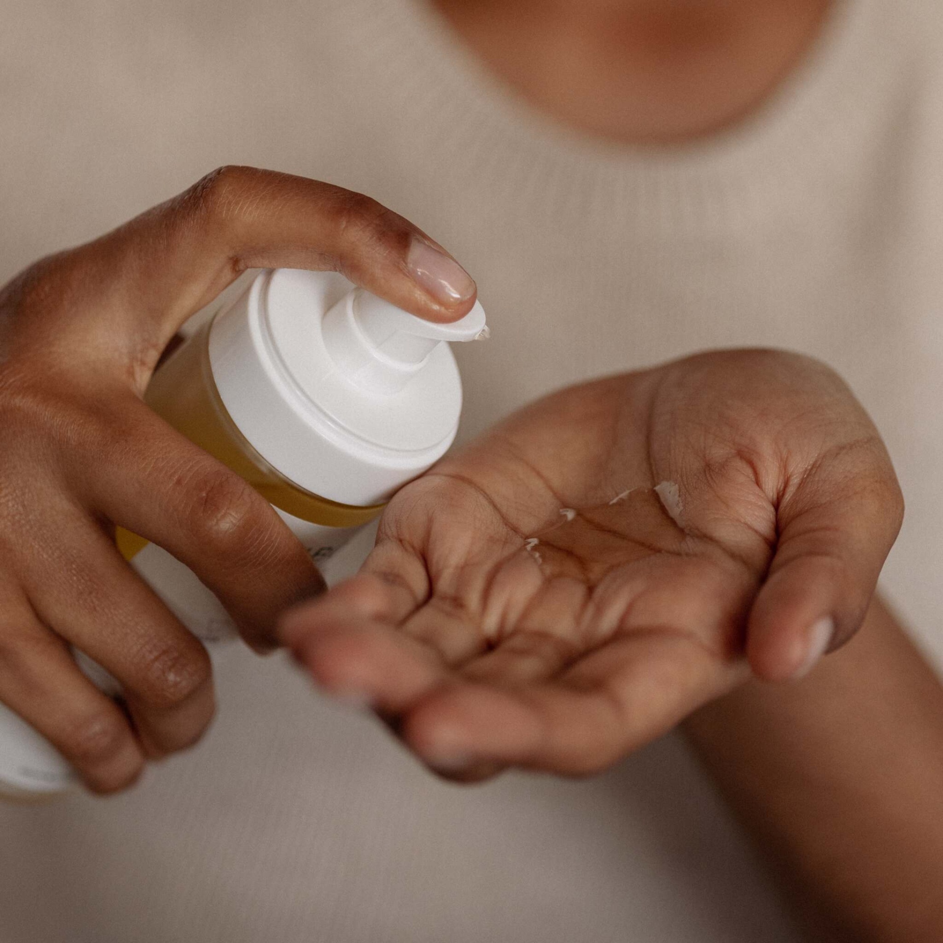 Mãos aplicando líquido com doseador branco num fundo neutro.