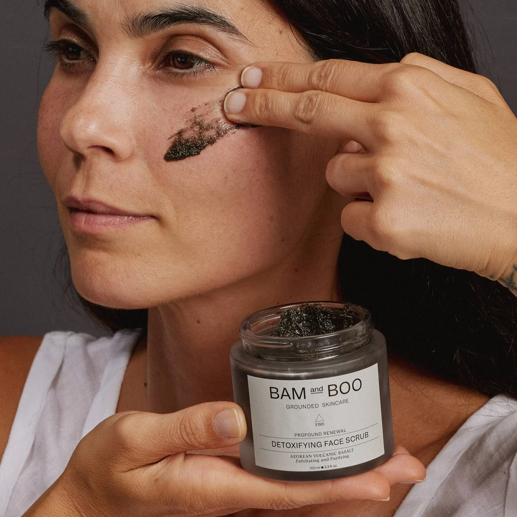 Mulher aplicando esfoliante facial preto BAM and BOO DETOXIFYING FACE SCRUB no rosto.
