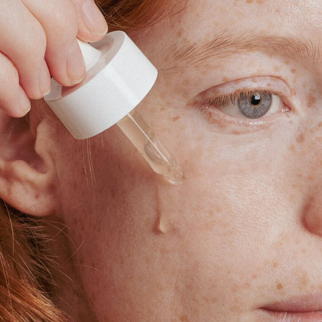 Pessoa aplicando produto líquido na pele com conta-gotas branco em close-up