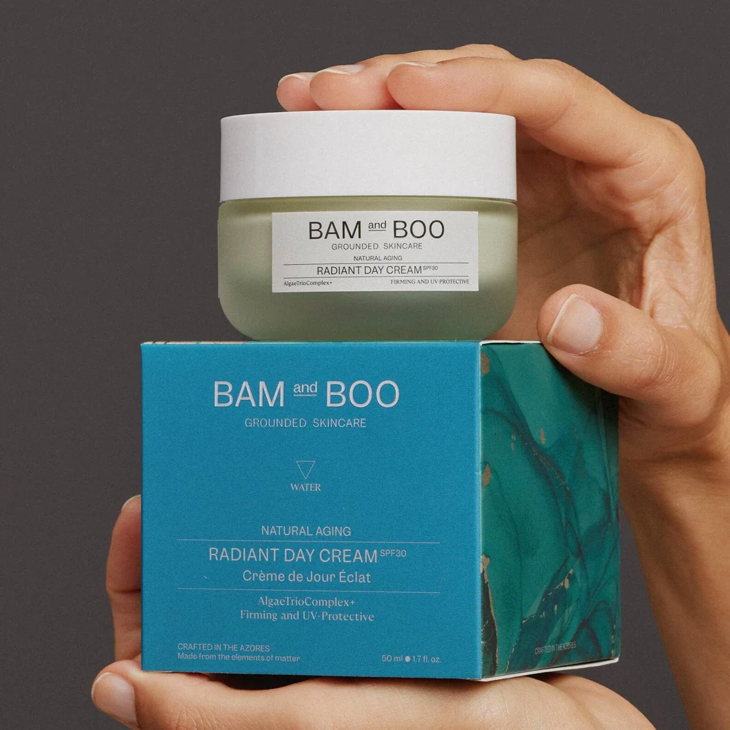 Frasco de creme facial BAM and BOO com caixa azul e mãos a segurá-los