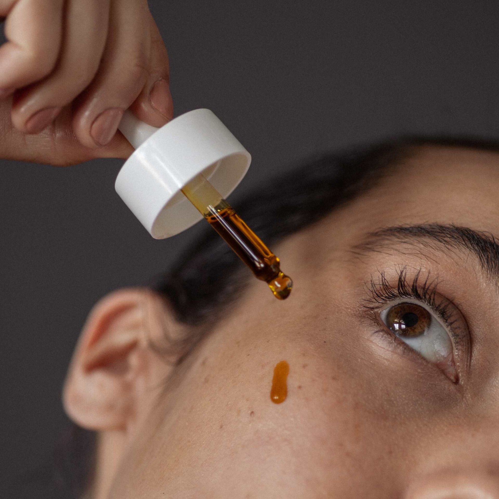 Conta-gotas branco a aplicar líquido ambar no rosto de pessoa com olhos castanhos