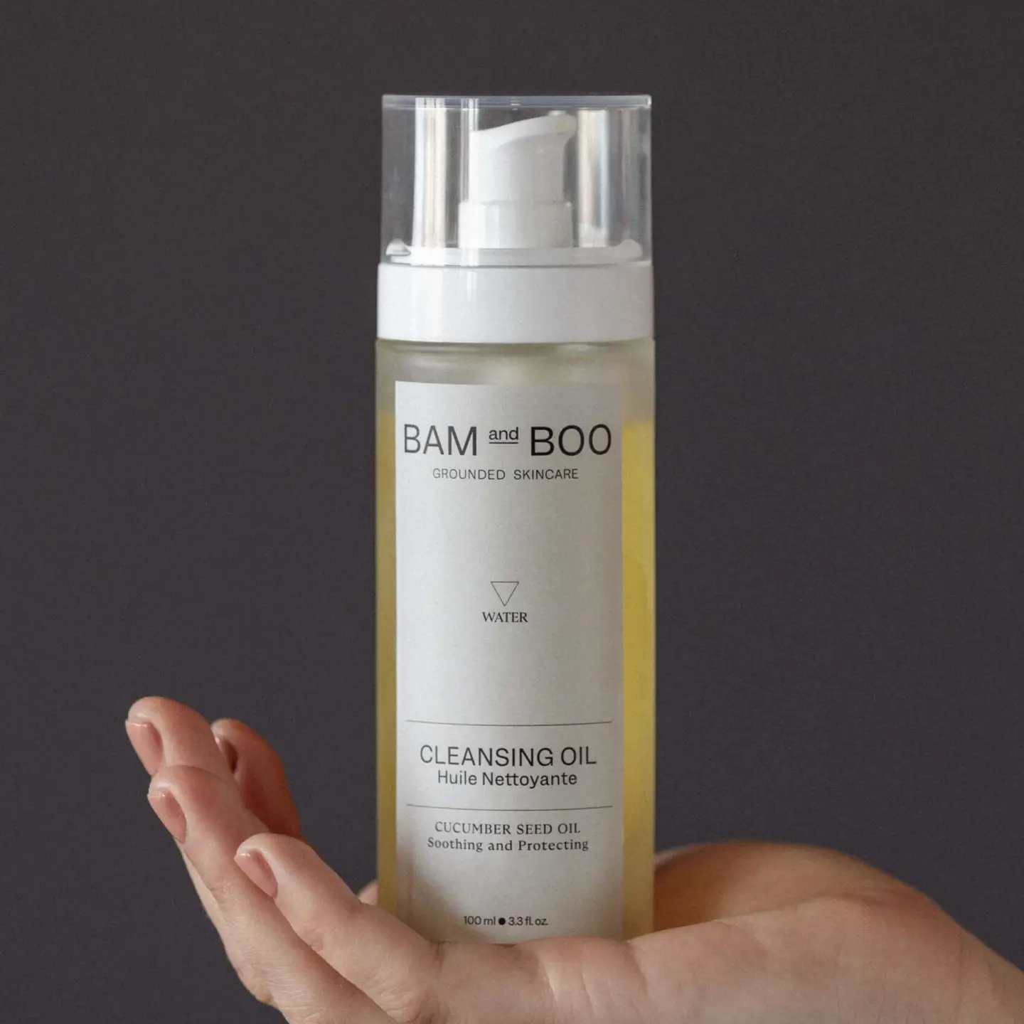 Frasco de óleo de limpeza com válvula de espuma e rótulo branco, segurado por uma mão