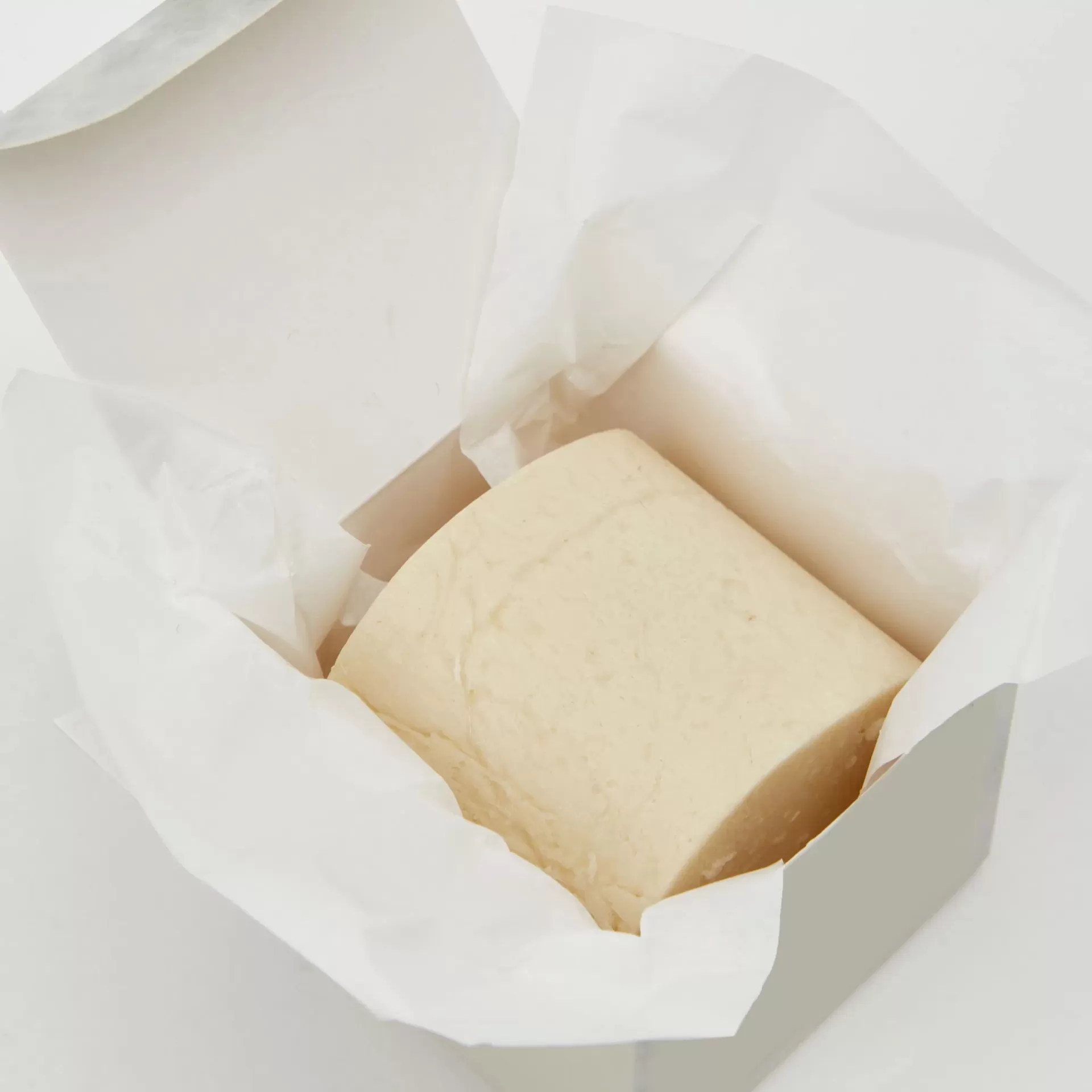 Bloco de queijo amarelo claro envolto em papel branco
