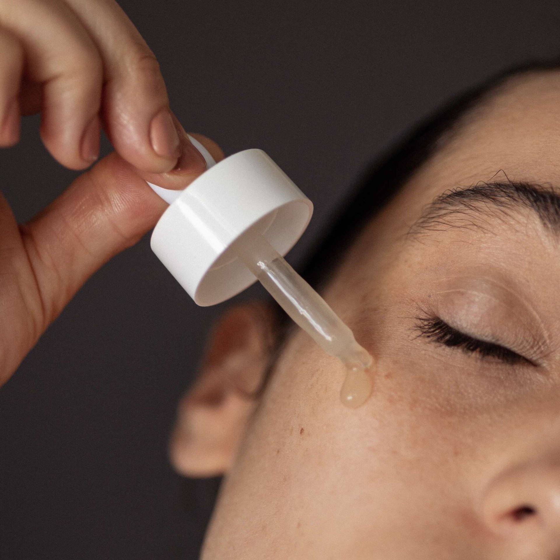 Pessoa aplicando sérum facial com conta-gotas branco na pele do rosto