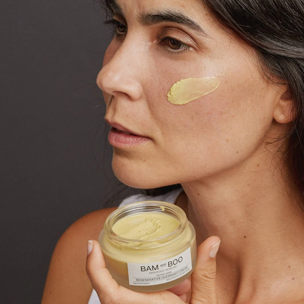 Mulher a aplicar creme BAM and BOO na face, produto em frasco de vidro aberto