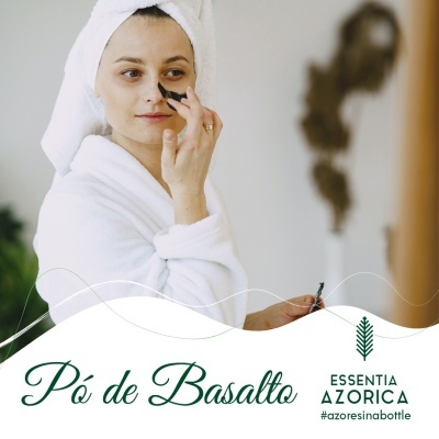 Mulher a aplicar máscara negra facial com toalha e roupão brancos.