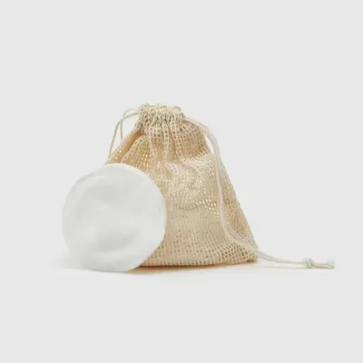 Disco de algodão branco redondo ao lado de saco de malha bege com fecho de cordão