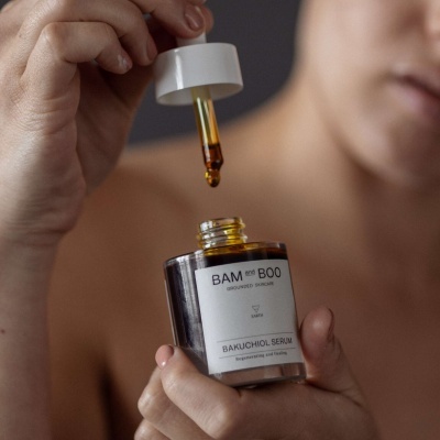 Frasco de seringa com sérum amarelo segurado por mãos com parte do rosto ao fundo.