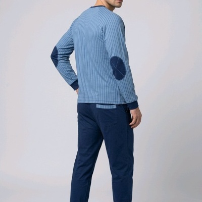Homem de pé com pijama azul claro e azul escuro num estúdio de fundo branco