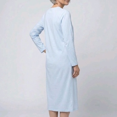 Mulher de costas com vestido azul claro comprido e chinelos brancos num fundo cinza.