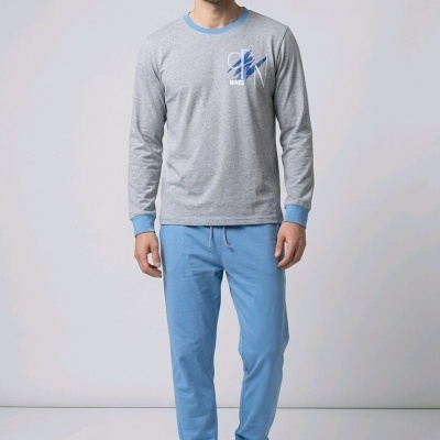 Homem com camisola cinza e azul e calças azuis num fundo neutro