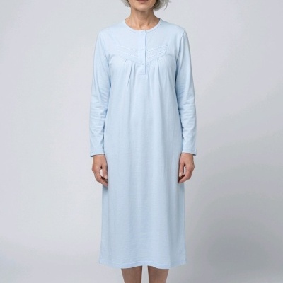 Camisola de dormir azul claro de manga comprida com botões e detalhe bordado no peito, usada por mulher de cabelo branco em fundo cinzento claro